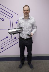 NYU Tandon Professor Justin Cappos, one of the leaders of the Uptane project, holds two of the automotive components that are vulnerable when automakers or mechanics update their software for recalls or performance modifications