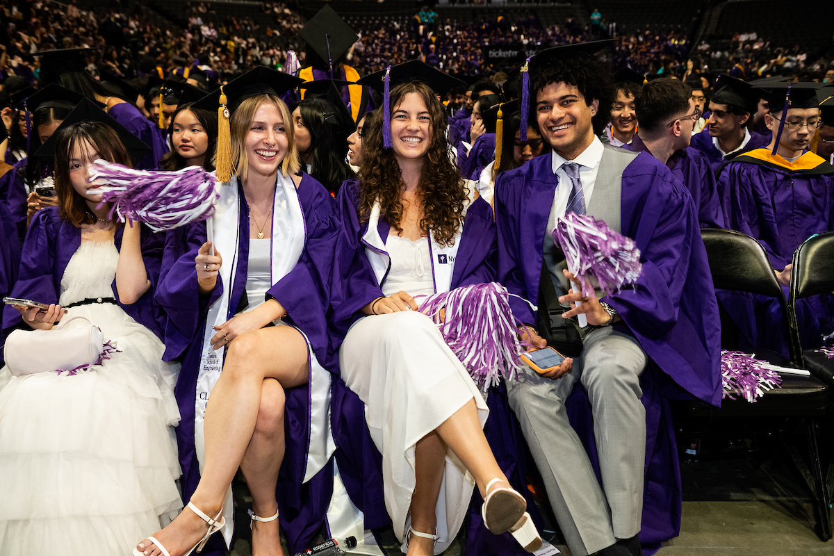 three smiling students in graduation robes holding pom poms at Graduation
