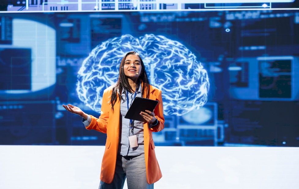 a young professional woman giving a presentation in front of a digital brain projected in background