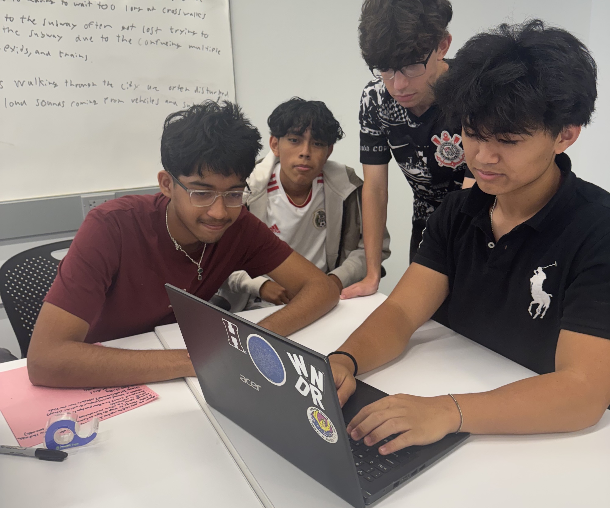four high school students huddled around a laptop