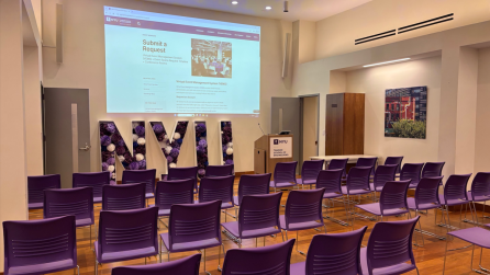 View from the back of the space, with four rows of ten chairs each in the image, facing a lectern and an image projected onto the wall.