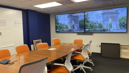 A room with a conference table with 10 chairs. At one end of the table there are two large displays.