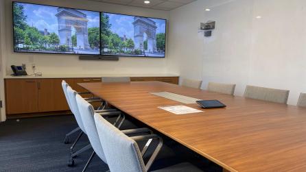 A room with a conference table with 10 chairs. At one end of the table there are two large displays.