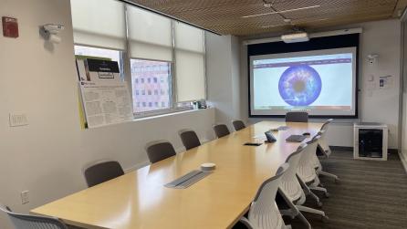 Image of a conference room with a table and twelve chairs, and a projector and screen at the end of the table.