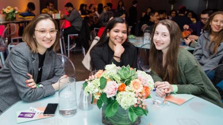 Three women sit smiling at a table in the event space
