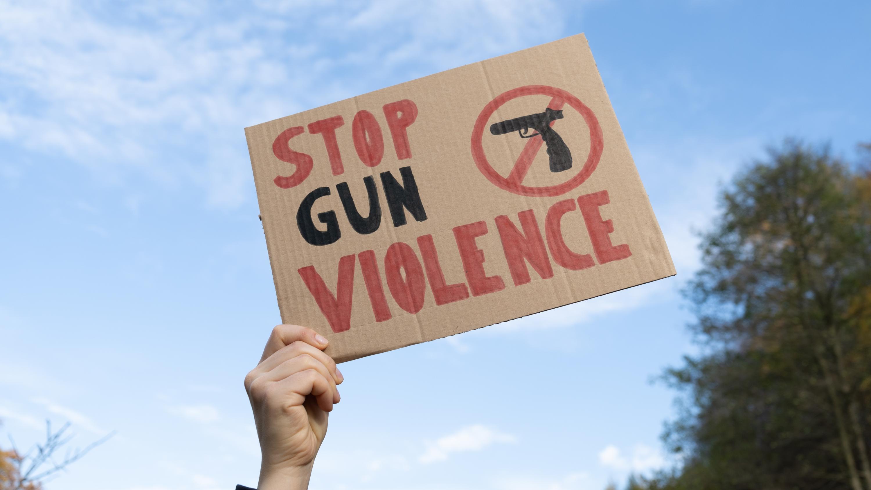hand holding cardboard sign stating stop gun violence