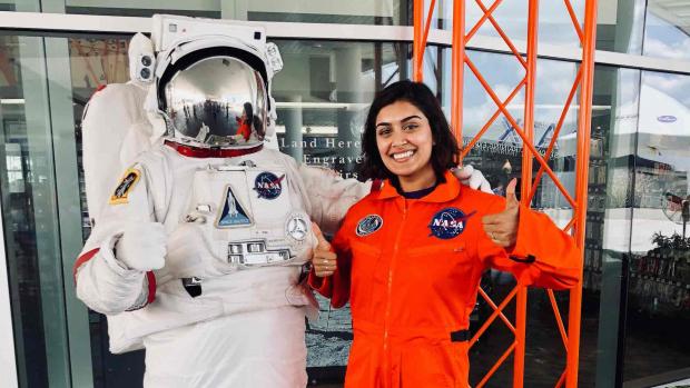 alum Tanya Gupta next to a space suit