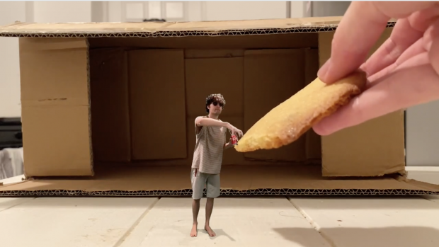 a still from a video showing a miniature student accepting a huge cookie