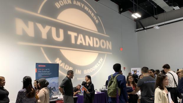 Large Tandon logo projected on wall at crowded career fair