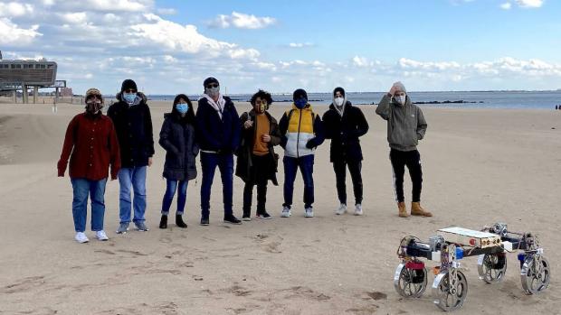 Student members of the Robotics team standing on the beach with the rover robot
