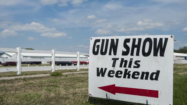 Awhite sign that says "Gun show this weekend" with a red arrow pointing to the left