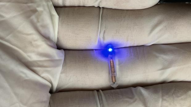 Gloved hand holding a small, pill-shaped electronic