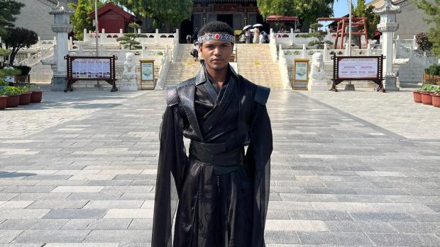 Student in traditional Chinese garments, standing in front of a building