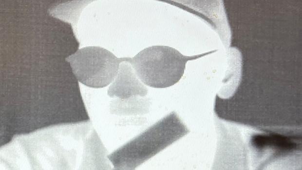 A close up infrared black and white image of a man wearing glasses and a baseball cap