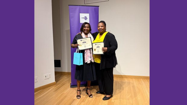 Two women holding certificates of service in front of Tandon banner