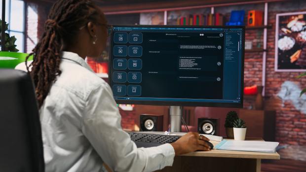 A person sits at a computer, interacting with an AI chat bot on the screen