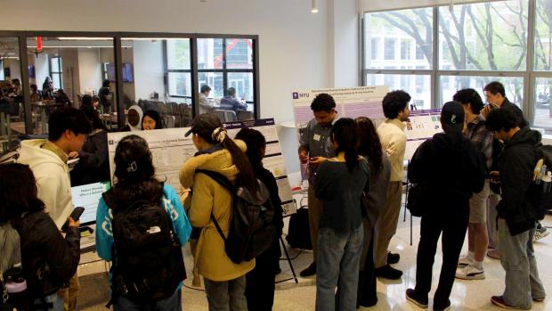 Students gathering around watching others present their 2026 Capstone poster boards in the MakerSpace Foyer