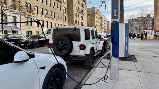 Two cars, a whie Jeep Wrangler and white Tesla being charged with plugNYC a electric vehicle charger.