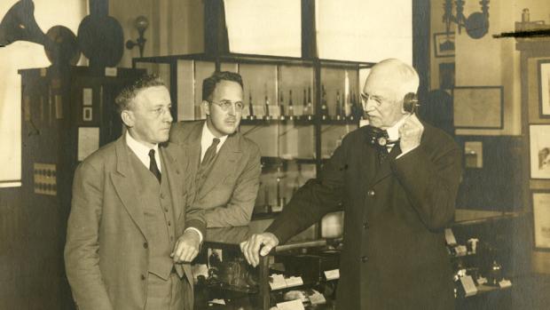 sepia toned photo of men in lab, one holding old telephone to ear
