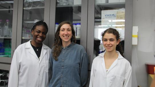 Professor Andrea Silverman flanked by two female students in the lab