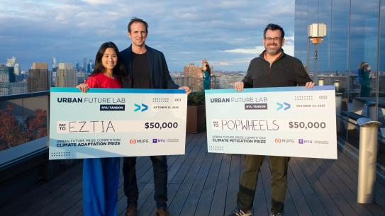 people holding oversized checks on an urban rooftop