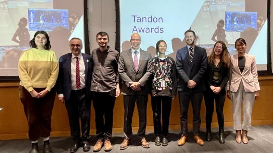 A group pose, smiling while standing in front of a screen that reads "Tandon Awards"