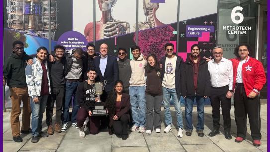 Students stand posing at the camera holding their first place trophey. 