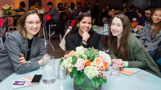 Three women sit smiling at a table in the event space