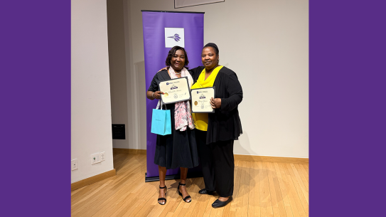 Two women holding certificates of service in front of Tandon banner