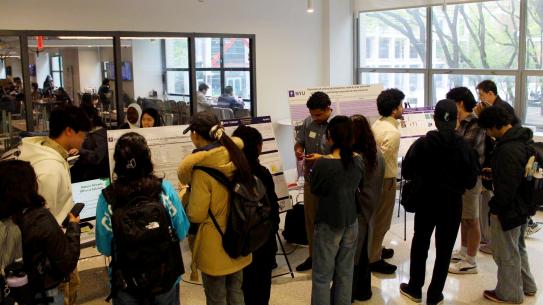 Students gathering around watching others present their 2026 Capstone poster boards in the MakerSpace Foyer