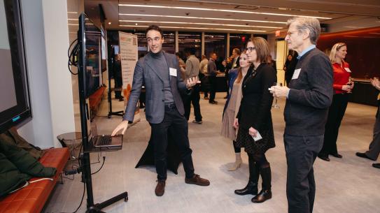 Andrea Gulisano leaning towards a propped TV screen, presenting work to Doreen Harris and Tone Søndergaard