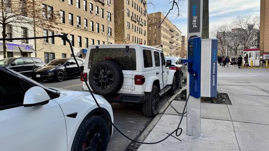 Two cars, a whie Jeep Wrangler and white Tesla being charged with plugNYC a electric vehicle charger.