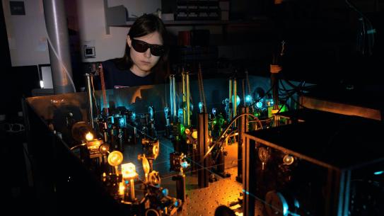 Amelia Klein wearing goggles behind a machine in a dark room.