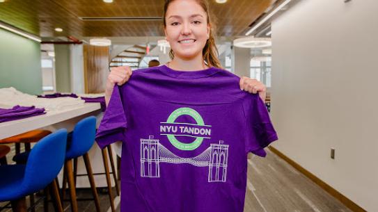 smiling student holding a Tandon T-shirt