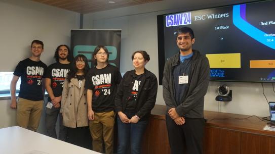 group of students wearing CSAW t-shirts standing in front of winners digital slide