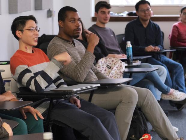 Phd Students sit in a discussion style classroom