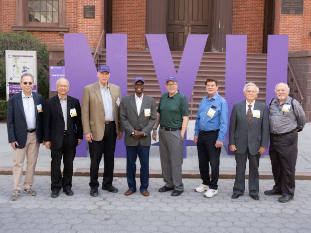 Group of alumni standing in front of oversized purple NYU letters
