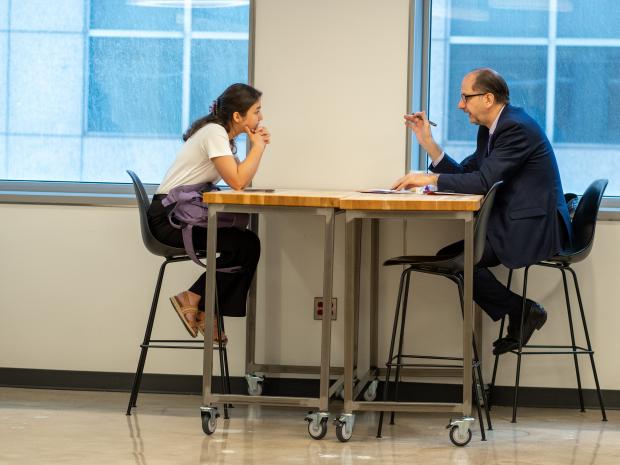 A student and faculty partner talk while sitting at a table. 