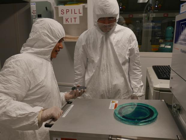 2 scientists in cleanroom garb talking over machinery