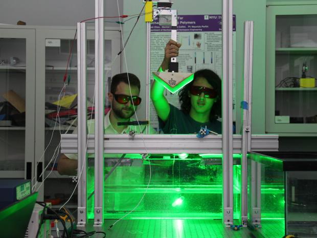 two students wearing saftey glasses in a lab with a glowing aquarium