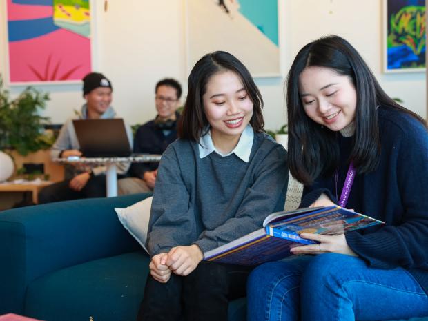 two girls sitting together, smiling while reading a textbook