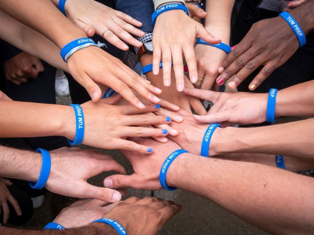 about a dozen hands with various skin tones wearing TUM PREP rubber bracelets
