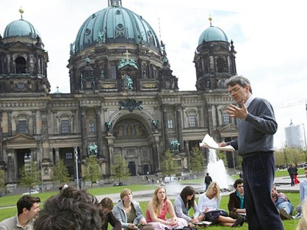 a class sitting outside on the greens with a cathedral in the background