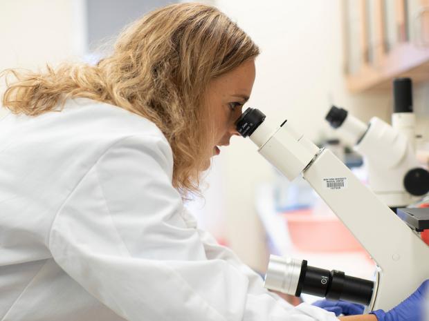 student wearing a lab coat looking into a microscope