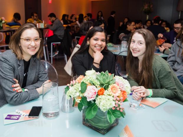 Three women sit smiling at a table in the event space