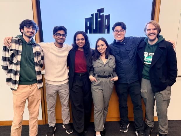 Six students smiling in front of a screen that reads AUSA