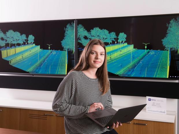 a female student holding a laoptop in front of digital screens