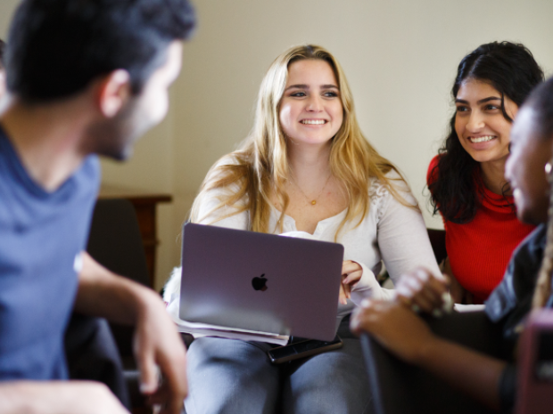 a smiling female student with a laptop on her lap surrounded by other students