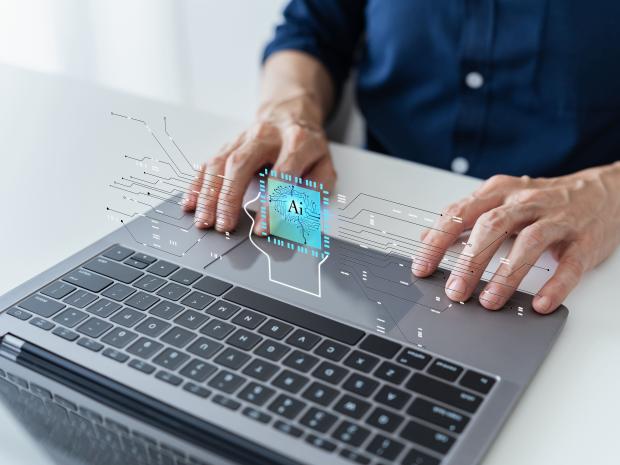 hands typing on laptop with "AI" superimposed 