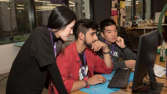 three students huddled over a laptop at CSAW